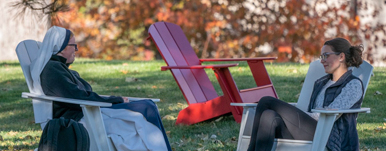 two women sitting in chairs on campus lawn