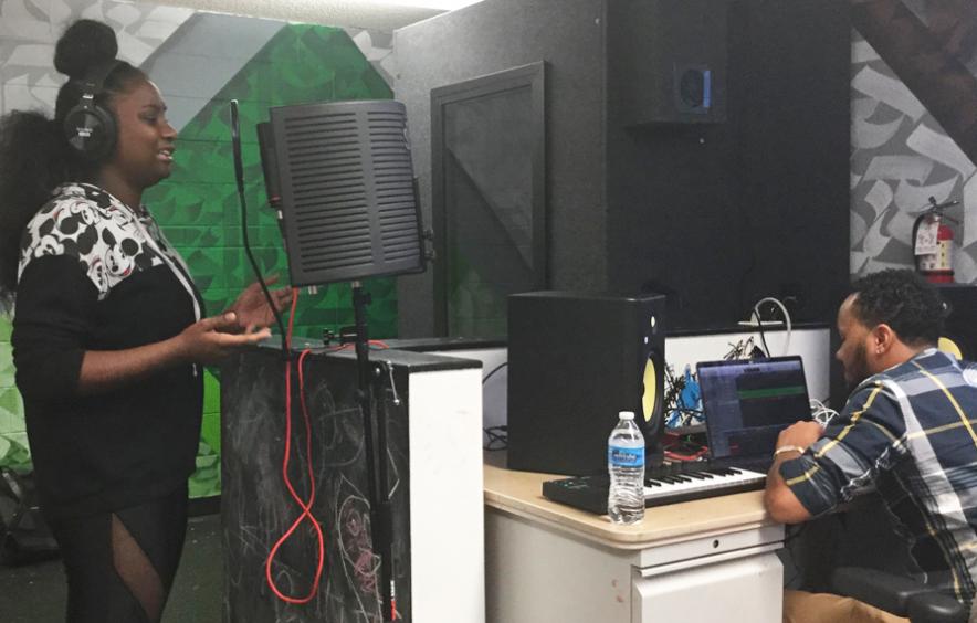 young black woman singing into mic at recording studio