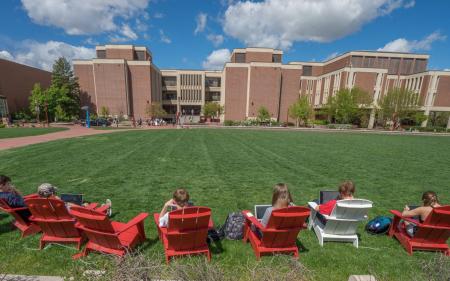 students in Adirondack chairs on a vast green lawn, all on laptop computers